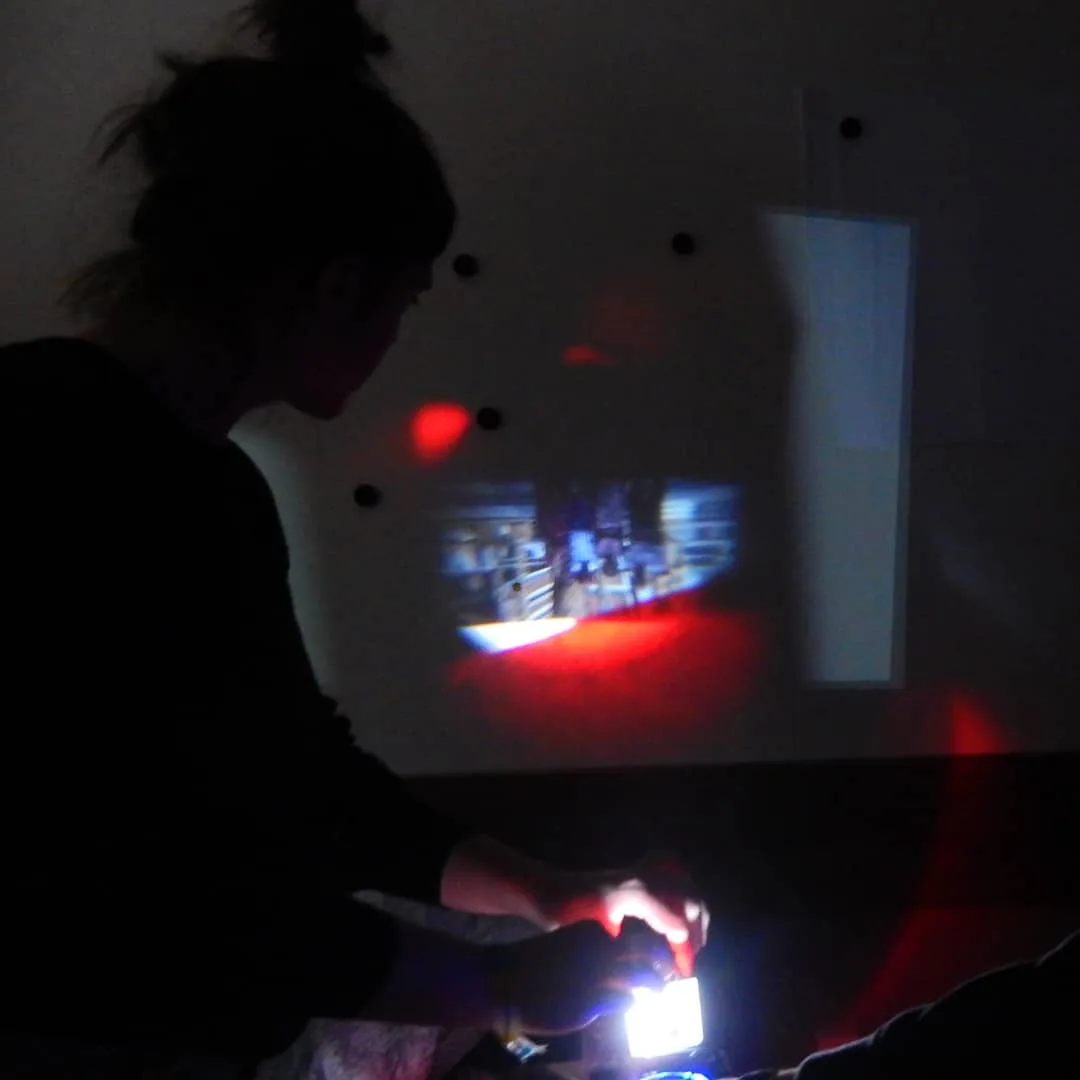 Una persona interactúa con un pequeño dispositivo de luz en una sala a oscuras.