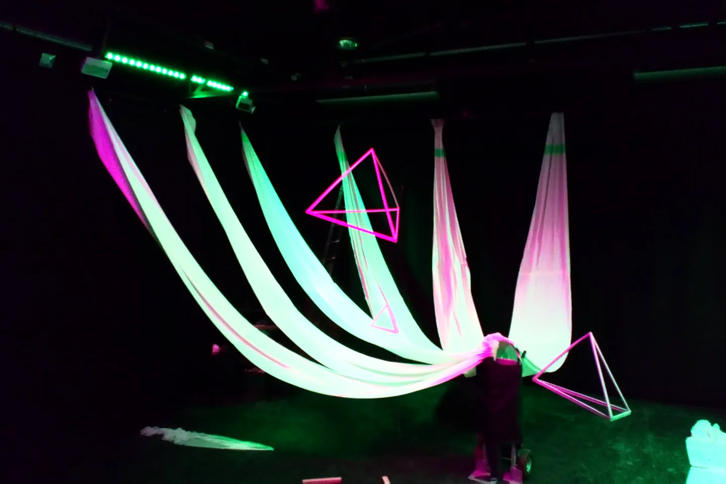 Tiras translúcidas y estructuras geométricas iluminadas en verde y magenta.