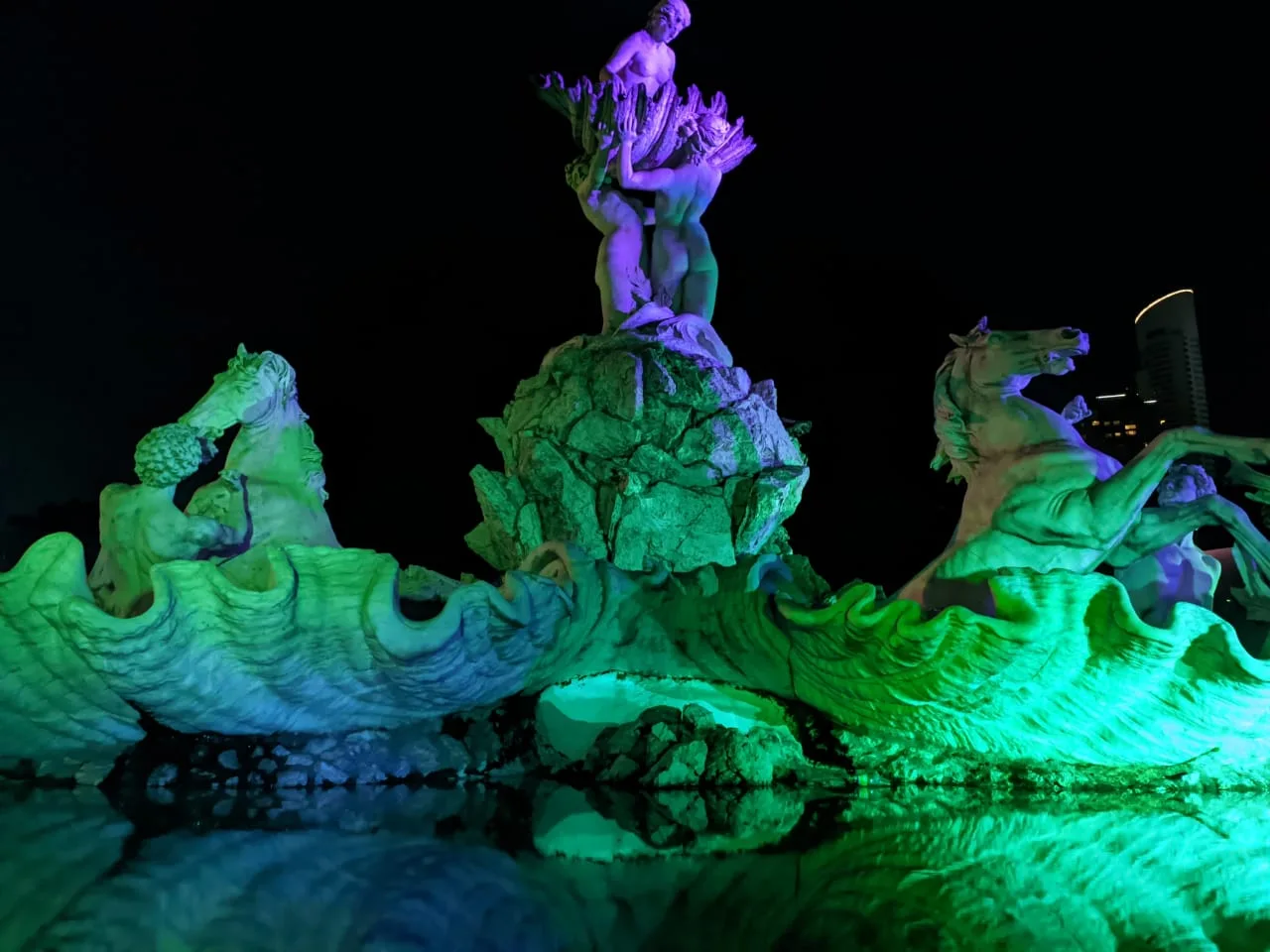 La Fuente de las Nereidas iluminada de verde y violeta durante una intervención nocturna.
